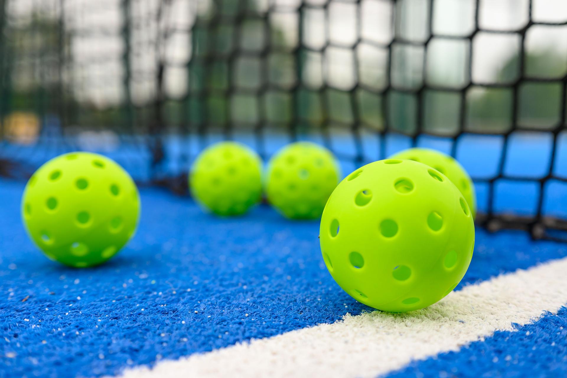 six pickleball balls near the net in a blue court, level surface view